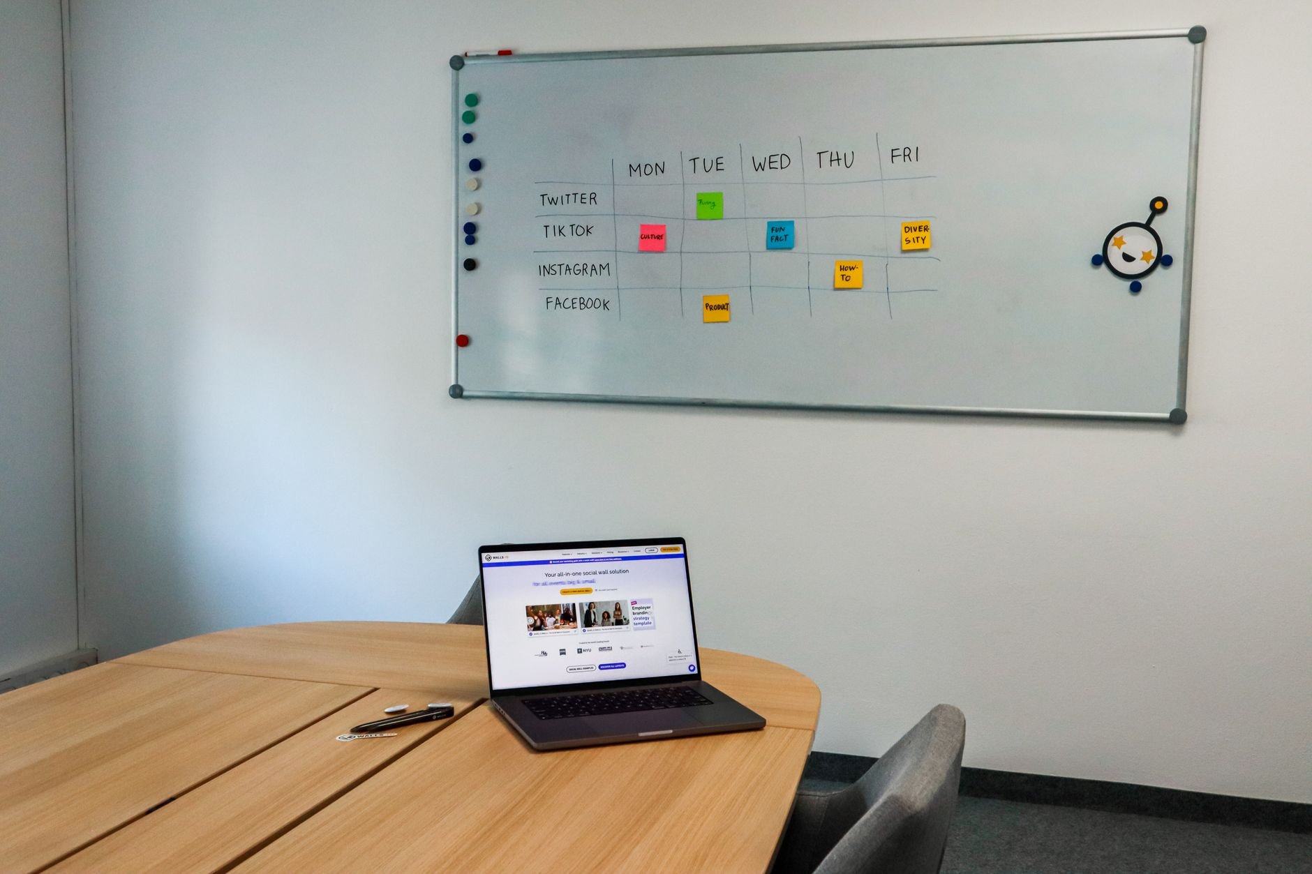 Office setup featuring a conference table, laptop, and organised whiteboard schedule.